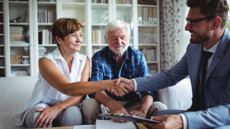 An investment advisor shaking a woman’s hand, who is sitting in her home alongside her husband